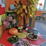 Spotkania dzieci z biblioteką - stół z ustawionymi na nim oznakami jesieni: Dynią, orzechami, grzybami, kasztanami, owocami i wazonem wypełnionym kolorowymi, jesiennymi liśćmi