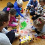 Spotkania dzieci z biblioteką - dzieci siedzą na ziemi i malują farbami rozłożony przed nimi arkusz folii bąbelkowej