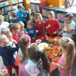 Spotkania dzieci z biblioteką - dzieci stoją przy stole i delektują się owocami i przyrządzonymi racuchami