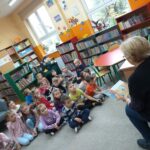 Dzieci w bibliotece z uwagą słuchają czytanej im bajki