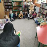 Dzieci siedzące w okręgu w bibliotece, słuchające z zaciekawieniem bajki