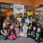 Zdjęcie grupowe dzieci w bibliotece z wielkimi pluszowymi maskotkami Kubusia Puchatka i Tygryska