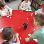 Dzieci przy stoliku w bibliotece wykonują pracę plastyczną z kolorowych kółek z papieru.