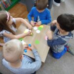 Dzieci przy stoliku w bibliotece wykonują pracę plastyczną z kolorowych kółek z papieru.