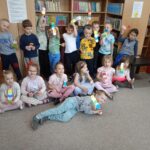 Pamiątkowe zdjęcie całej grupy przedszkolaków biorących udział w zajęciach na tle półki z książkami