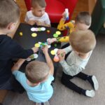 Dzieci przy stoliku w bibliotece wykonują pracę plastyczną z kolorowych kółek z papieru.
