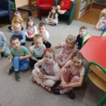 Dzieci siedzą na podłodze w bibliotece i z uwagą słuchają czytanej bajki