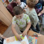 Chopak przykleja wykonany przez siebie "dymek" na okładkę grubej książki, która zatytułowana jest "Wspomnienia z przedszkola"