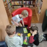 Troje dzieci klęcząc przy niskim, kwadratowym stole wykonuje prace plastyczne - na karteczkach w kształcie komiksowych "dymków" rysuje swoje wspomnienia z przedszkola