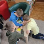 Trzech chłopców klęczy przy niskim, kwadratowym stole pisząc coś na żółtych karteczkach
