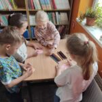 Czworo dzieci stojąc przy kwadratowym stole wykonuje prace plastyczne - na karteczkach w kształcie komiksowych "dymków" rysuje swoje wspomnienia z przedszkola