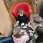 Czworo dzieci klęcząc przy niskim, kwadratowym stole wykonuje prace plastyczne - na karteczkach w kształcie komiksowych "dymków" rysuje swoje wspomnienia z przedszkola