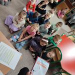 Dzieci siedzą na ziemi i z uwagą słuchają opowiadania o bocianie