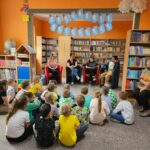 Spotkanie autorskie - dzieci siedzą na podłodze i uważnie słuchają czytanego przez rodziców opowiadania