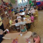 Dzieci przy stolikach wykonują pracę plastyczną - z tekturowego talerzyka przeciętego na pół i doklejonych do niego nóżek z kolorowej bibuły - tworzą "ośmiornice"