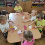 Dzieci przy stolikach wykonują pracę plastyczną - z tekturowego talerzyka przeciętego na pół i doklejonych do niego nóżek z kolorowej bibuły - tworzą "ośmiornice"