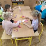 Dzieci przy stolikach wykonują pracę plastyczną - z tekturowego talerzyka przeciętego na pół i doklejonych do niego nóżek z kolorowej bibuły - tworzą "ośmiornice"