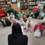 Dzieci siedzą na ziemi i uważnie słuchają opowiadania