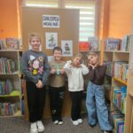 Grupa chłopaków w sali biblioteki stoi na tle półek z książkami