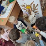 Dzieci przyklejają kolorowe liście do konarów i gałęzi drzewa jako praca plastyczna