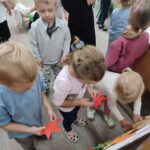 Dzieci przyklejają kolorowe liście do konarów i gałęzi drzewa jako praca plastyczna