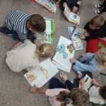 Grupa dzieci siedzi na podłodze w sali biblioteki i przegląda wybrane książki