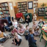 Dzieci siedzą na podłodze sali biblioteki i aktywnie uczestniczą w zajęciach