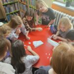 Dzieci przy czerwonym stoliku przygotowują pracę plastyczną