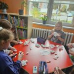Dzieci przy czerwonym stoliku przygotowują pracę plastyczną