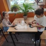Dzieci przy stoliku wykonują pracę plastyczną - czarnego kota
