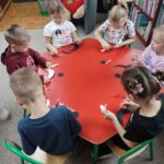 Dzieci przy stoliku wykonują pracę plastyczną - czarnego kota