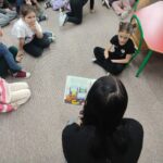 Dzieci siedzą na ziemi i z uwagą słuchają bajki