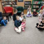 Dzieci siedzą na ziemi i z uwagą słuchają bajki