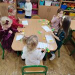 Przedszkolaki siedzą przy stole i wykonują pracę plastyczną