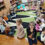 Dzieci siedzą na podłodze i z uwagą słuchają opowiadania o jeżu