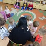 Dzieci siedzą na podłodze i z uwagą słuchają opowiadania