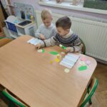 Przedszkolaki siedzą przy stole i wykonują pracę plastyczną