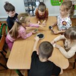 Dzieci siedzą przy stole i wykonują pracę plastyczną - jeżyki.