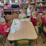 Przedszkolaki siedzą przy stole i wykonują pracę plastyczną