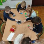 Dzieci siedzą przy stole i wykonują pracę plastyczną - jeżyki.