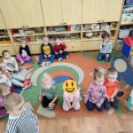 Dzieci siedzą na podłodze i z uwagą słuchają opowiadania