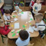 Przedszkolaki siedzą przy stole i wykonują pracę plastyczną