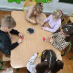 Dzieci siedzą przy stole i wykonują pracę plastyczną - jeżyki.