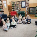 Dzieci siedzą na ziemi i z uwagą słuchają opowiadania