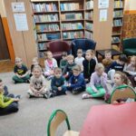 Przedszkolaki siedzą na podłodze i z uwagą słuchają opowiadania czytanego przez nauczyciela