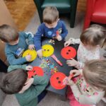 Dzieci przy stolikach wykoują pracę plastyczną - ozdabiają papierowe guziki