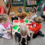 Dzieci przy stolikach wykoują pracę plastyczną - ozdabiają papierowe guziki