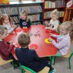 Dzieci przy stolikach wykoują pracę plastyczną - ozdabiają papierowe guziki