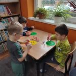 Dzieci przy stolikach wykoują pracę plastyczną - ozdabiają papierowe guziki