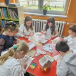 Dzieci przy stoliku wykonują pracę plastyczną